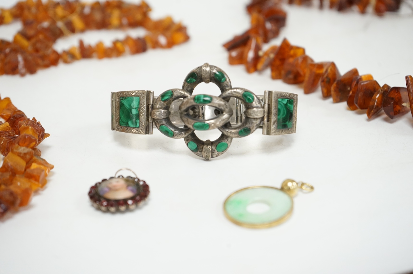 An early to mid 20th century engraved white metal and malachite set 'knot' bracelet, together with a Victorian garnet and enamel portrait pendant, a mounted jadeite disc pendant and two amber necklaces.